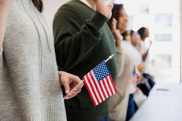 Lidé držící malé americké vlajky během ceremonie, s rukama zvednutými v gestu přísahy