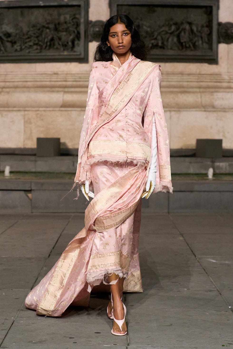 Modelka předvádějící elegantní růžový outfit s detailním zdobením na přehlídce